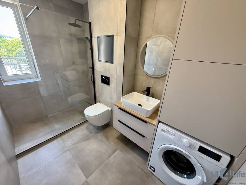 Badezimmer in einer 2-Zimmer-Wohnung mit Waschmaschine, Dusche und Fenster.