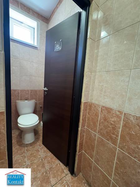 Toilette mit geschlossener Tür in Geschäftsräumen, gefliest mit braunen Fliesen.
