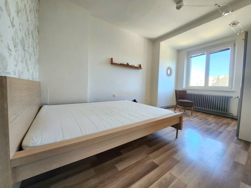 Schlafzimmer in einer 2-Zimmer-Wohnung mit Holzboden, Bett und Sessel.