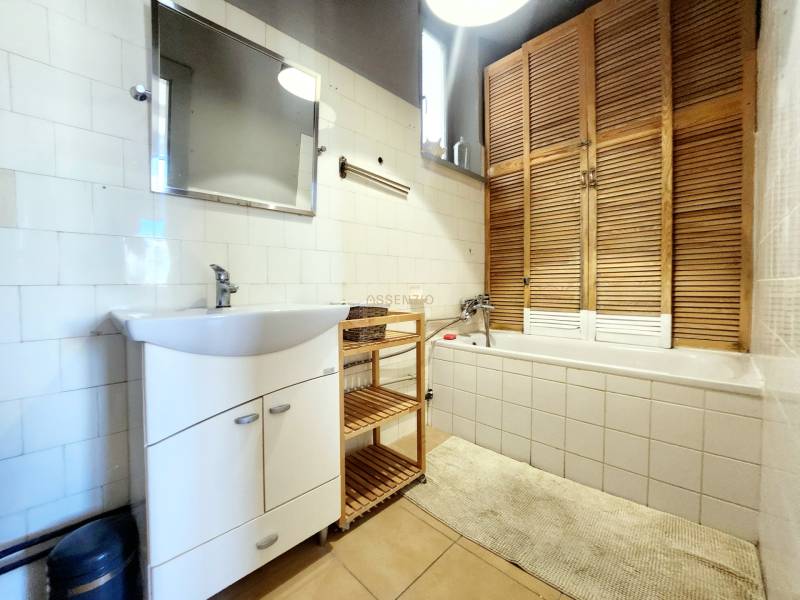 Badezimmer in einer 2-Zimmer-Wohnung mit Badewanne, Waschbecken und einem Holzschrank.