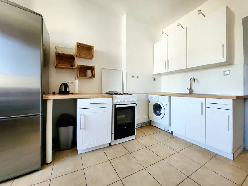 Küche in einer 2-Zimmer-Wohnung mit Geräten und minimalistischen Holzmöbeln.