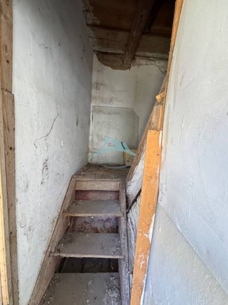 Eine enge Holztreppe in Geschäftsräumen mit weißen Wänden und einer Balkendecke.
