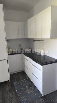 Küche in einer 2-Zimmer-Wohnung mit weißen Schränken und dunkler Arbeitsplatte.