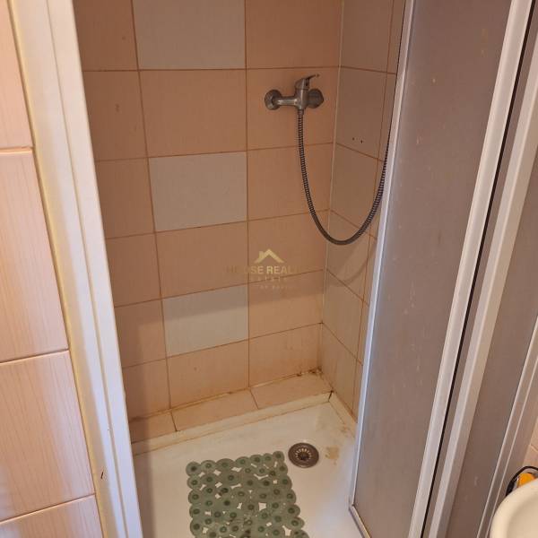 Duschkabine in einer Einzimmerwohnung mit Fliesen und einem Wasserschlauch.