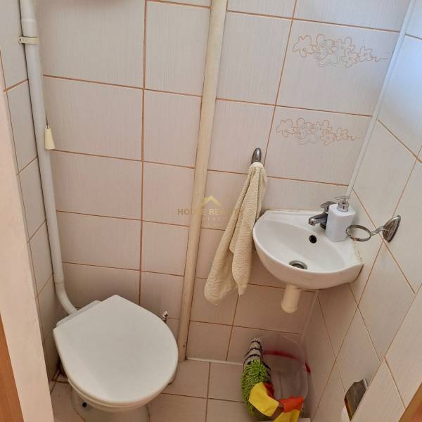 Toilette und Waschbecken im Badezimmer einer Einzimmerwohnung mit beigen Fliesen.