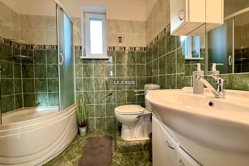 Badezimmer in einem Einfamilienhaus mit grünen Fliesen, einer Duschkabine und einem Waschbecken.
