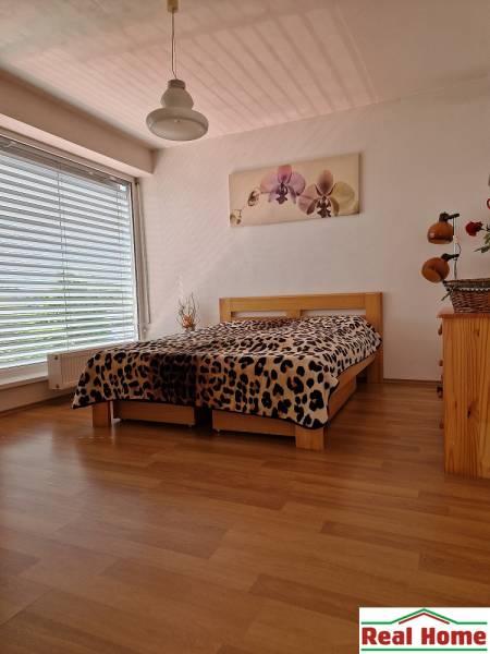 Schlafzimmer in einem Einfamilienhaus mit großem Fenster, Bett und Bild an der Wand.