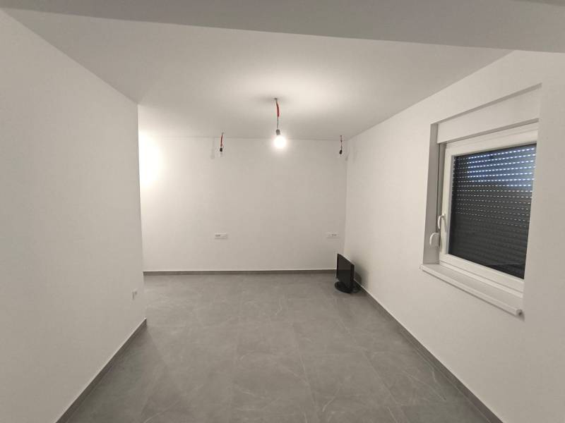Ein leerer Raum in einer Vierzimmerwohnung mit weißen Wänden und grauem Boden.