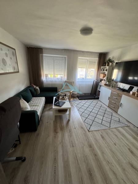 Wohnzimmer in einer 3-Zimmer-Wohnung mit Sofa, Tisch, Fernseher und Teppichboden.