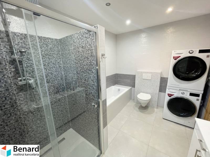 Ein Badezimmer in einem Einfamilienhaus mit Badewanne, Dusche und Waschmaschine mit Trockner.
