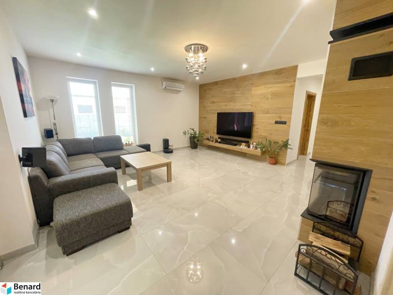 Wohnzimmer in einem Einfamilienhaus mit Kamin, Ecksofa und Fernseher an der Holzwand.