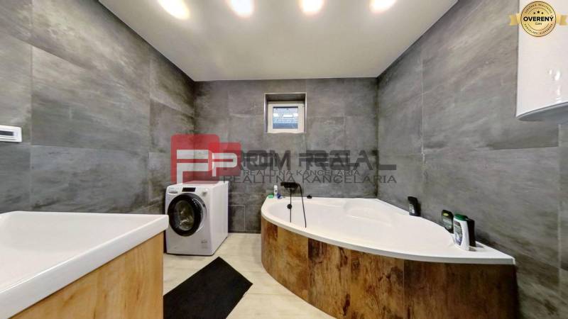 Badezimmer mit Badewanne und Waschmaschine in einem Einfamilienhaus. Graue Wände mit hellen Böden.