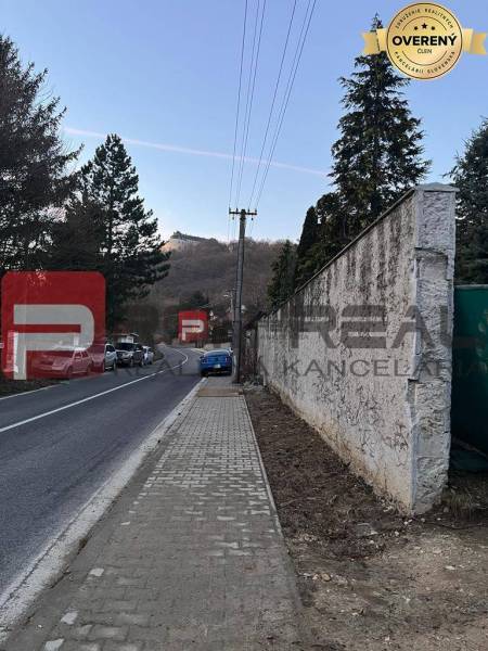 Ein Weg mit einem Gehsteig, der durch Pezinok an einem Einfamilienhaus vorbeiführt, im Hintergrund eine hügelige Landschaft.