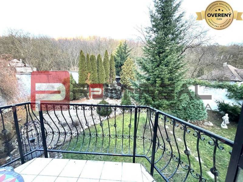 Der Garten des Einfamilienhauses in der Gemeinde Píla mit Ziergehölzen und einem schmiedeeisernen Geländer.