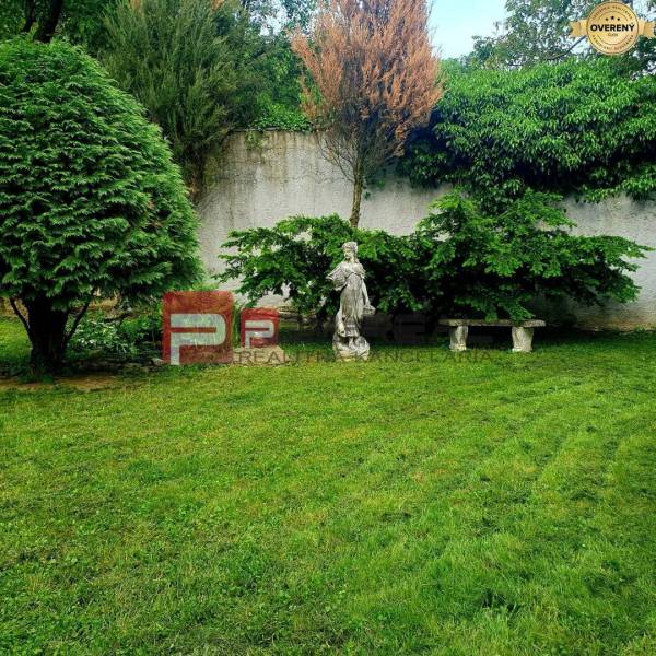 Der Garten eines Einfamilienhauses in der Gemeinde Píla mit Rasen, einer Statue und einer Bank an der Wand.