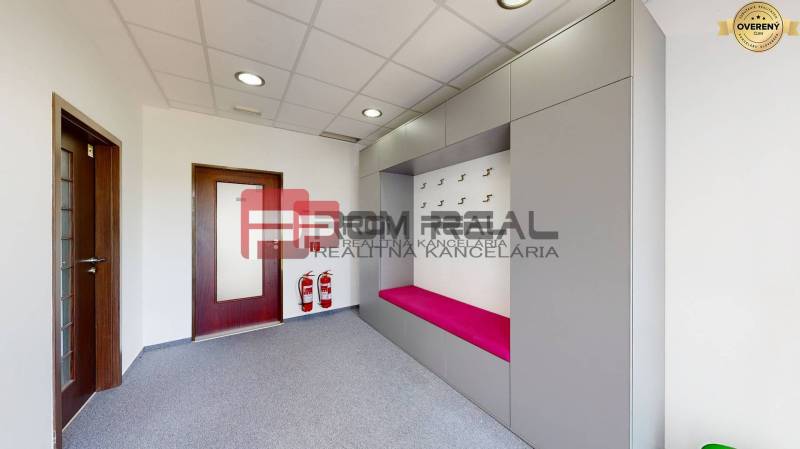 Innenraum eines Büros mit einer Garderobenwand, einer rosa Bank und Brandschutzausrüstung.