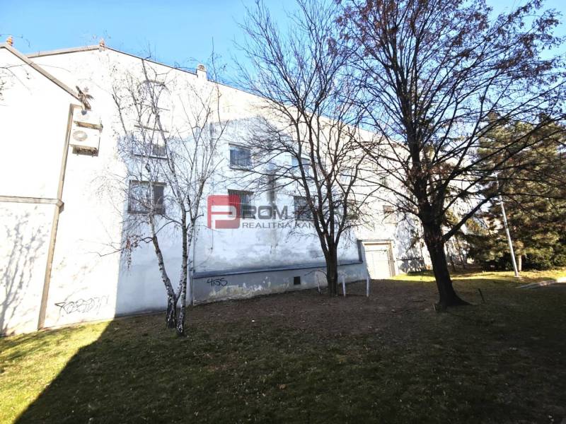 Ein Gebäude mit Grünflächen und Bäumen in der Ľ. Podjavorinská Straße, im Hintergrund ein blauer Himmel.