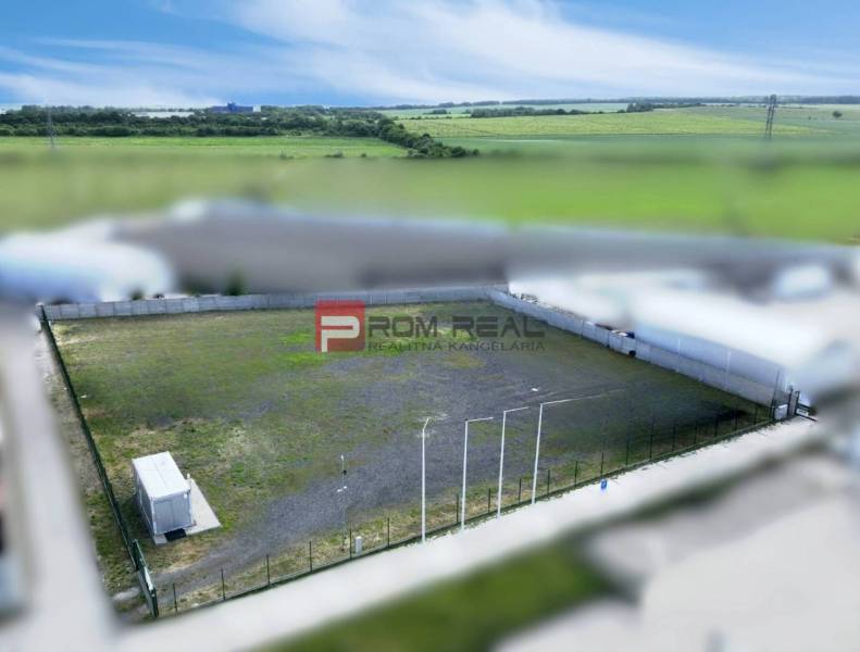 Produktionsräume in Pezinok mit eingezäuntem Außenbereich und Container, umgeben von Feldern.