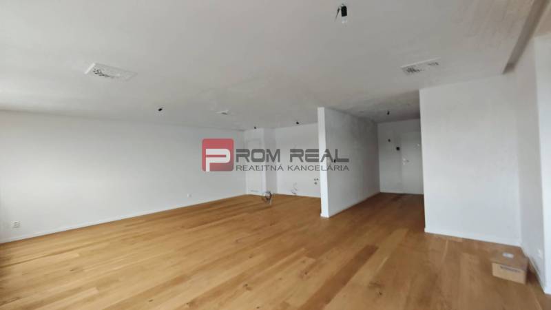 Ein geräumiges Zimmer mit Holzboden in einer 4-Zimmer-Wohnung, helle Wände und eine einfache Einrichtung.