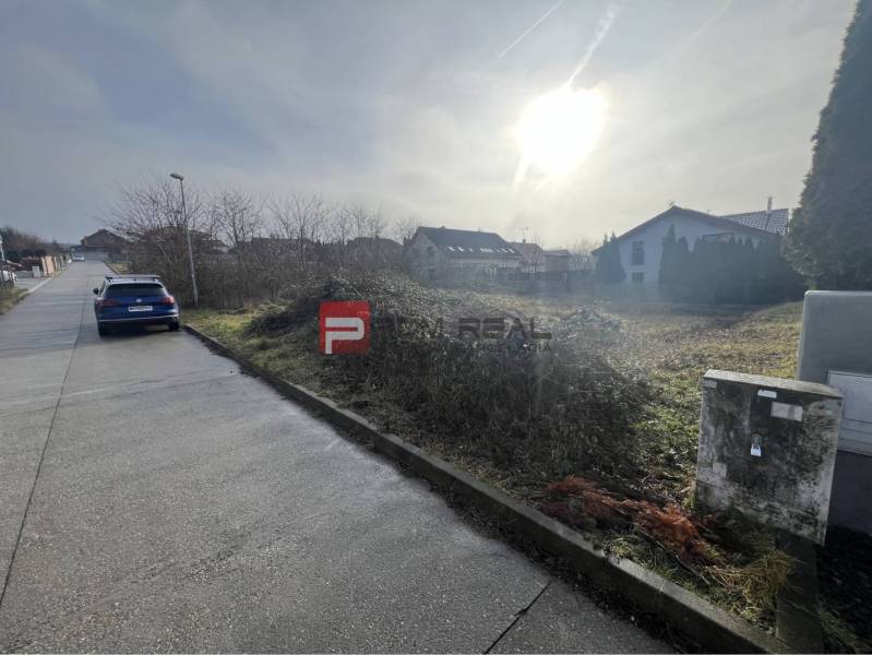 Baugrundstück in Stupava in der Bazova-Straße, sonnige Umgebung und Auto an der Straße.