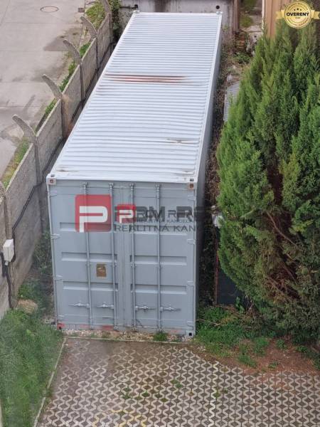 An der Púchovská-Straße in Bratislava III befindet sich ein Schiffscontainer neben Grünflächen und einem Zaun.