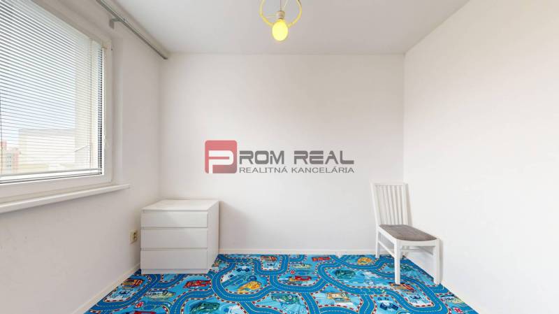 Ein leerer Raum mit einem bunten Teppich, einem Stuhl und einer Kommode in einer 4-Zimmer-Wohnung.
