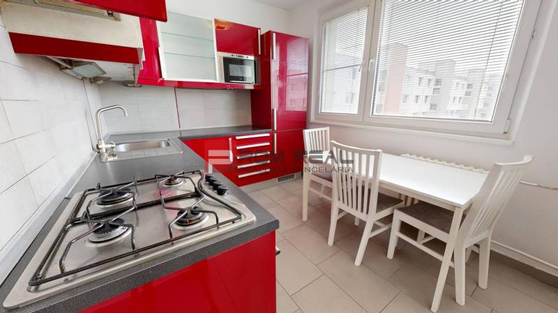 Die Küche einer 4-Zimmer-Wohnung mit roten Schränken, einem Gasherd und einem Esstisch.