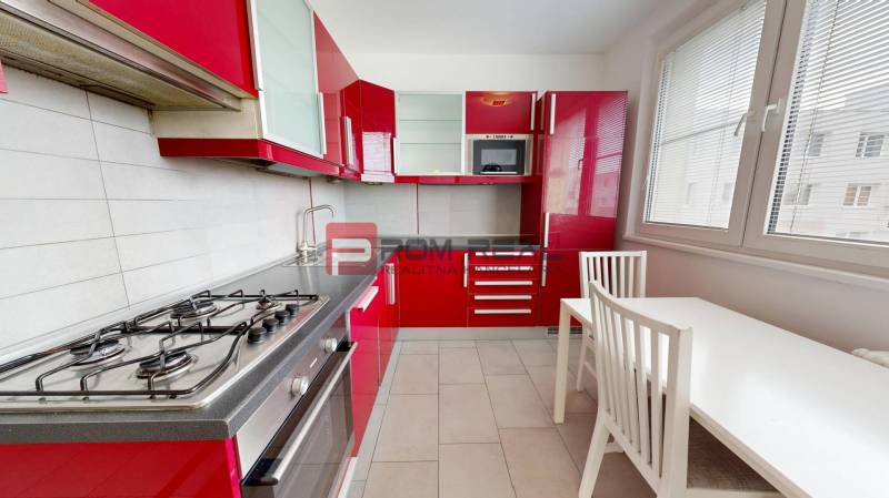 Eine Küche mit roten Schränken, einem Gasherd und einem weißen Esstisch in einer Vierzimmerwohnung.