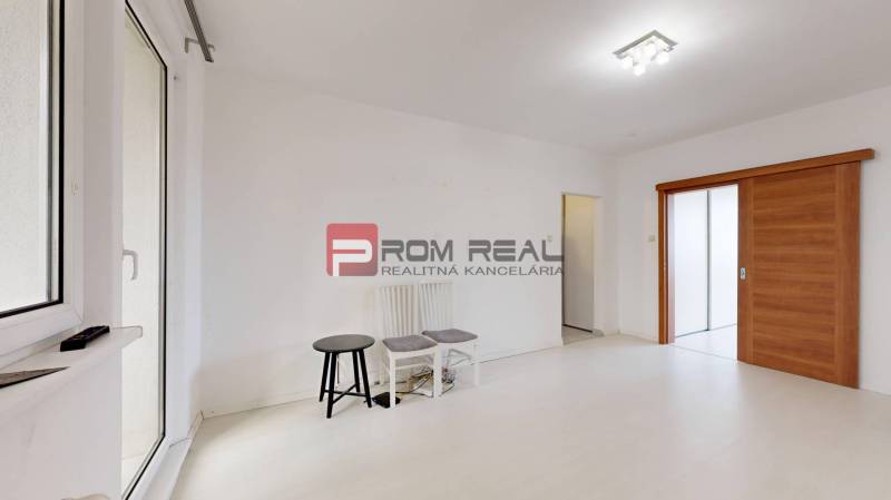 Helles Zimmer mit weißen Wänden, Schiebetüren aus Holz und zwei Stühlen in einer Vierzimmerwohnung.
