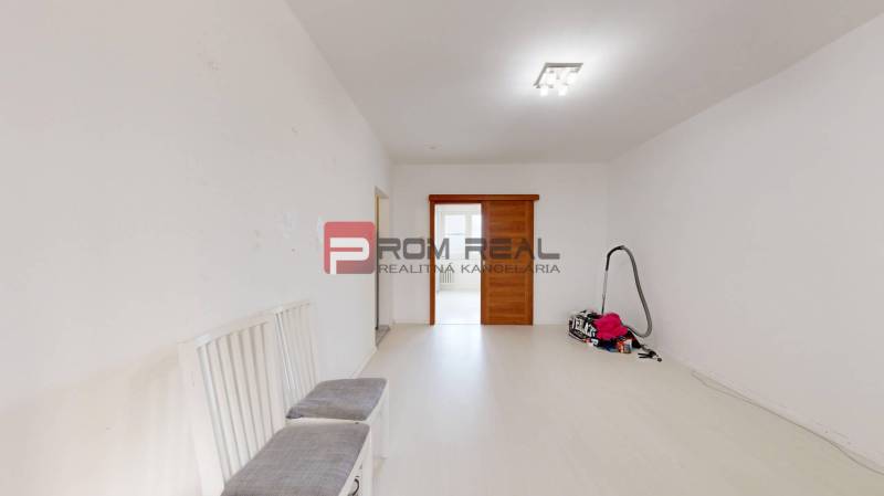 Ein heller Raum in einer 4-Zimmer-Wohnung mit Schiebetüren und Stühlen. Ein abgestellter Staubsauger auf dem Boden.