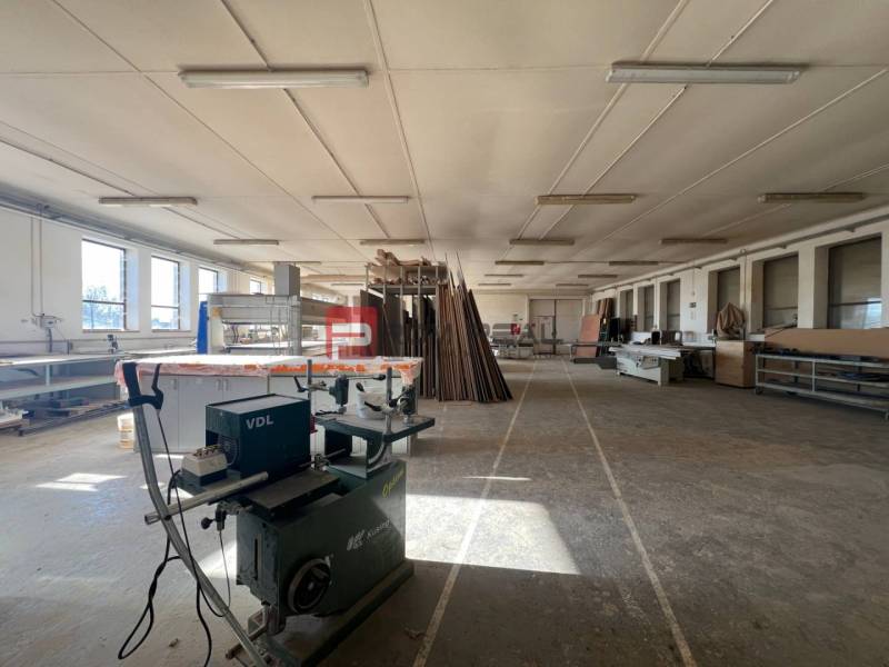 Produktionsräume mit Holzbearbeitungsmaschine und Materialien, ausreichend natürliches Licht.