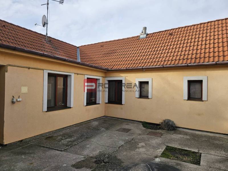 Der Hof des Einfamilienhauses in der Sonnenstraße in Pezinok mit Betonpflaster und orangefarbener Fassade.