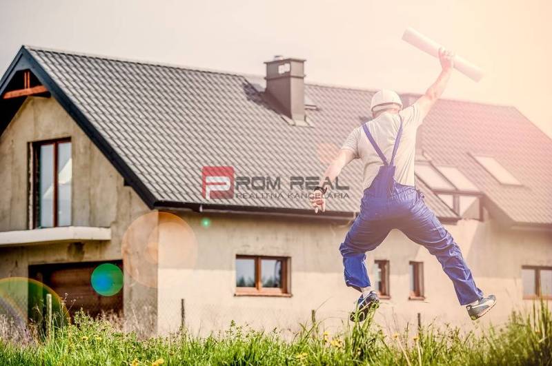 Der Bauarbeiter springt glücklich vor dem Haus und hält die Baupläne. Bau und Einzimmerwohnung.