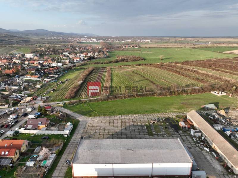 Luftaufnahme von Vinosady von der Pezinska-Straße, umgeben von Weinbergen und Produktionsanlagen.