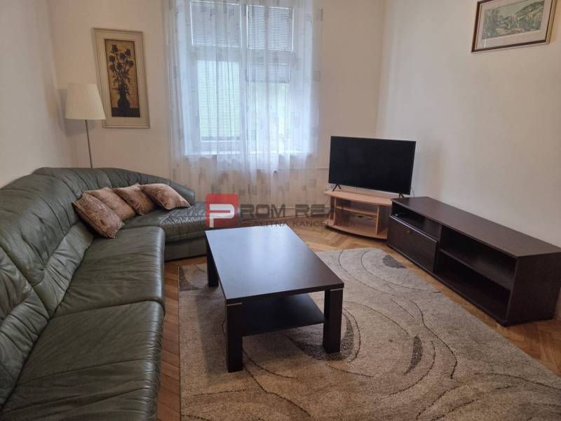 Wohnzimmer mit Ecksofa, Fernseher und Couchtisch in einer Zweizimmerwohnung.