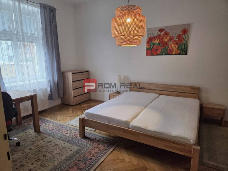 Schlafzimmer mit einem Holzbett, einem Schreibtisch und heller Dekoration in einer 2-Zimmer-Wohnung.