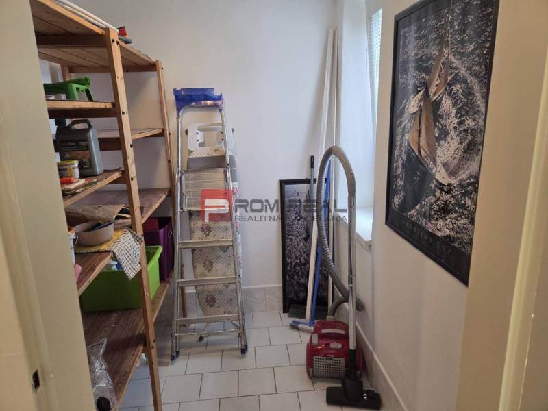Stauraum in einer 2-Zimmer-Wohnung mit Regalen, Staubsauger und Leiter.