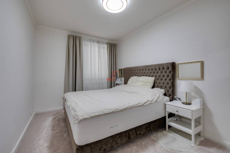Schlafzimmer in einer 3-Zimmer-Wohnung mit einem bequemen Bett, einem Nachttisch und Vorhängen.