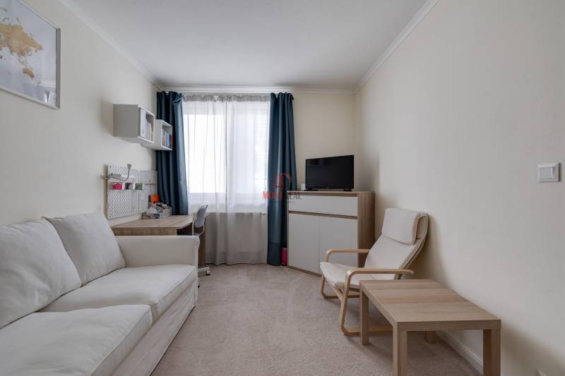 Wohnzimmer in einer 3-Zimmer-Wohnung mit einem bequemen Sofa, einem Sessel und einem Schreibtisch.