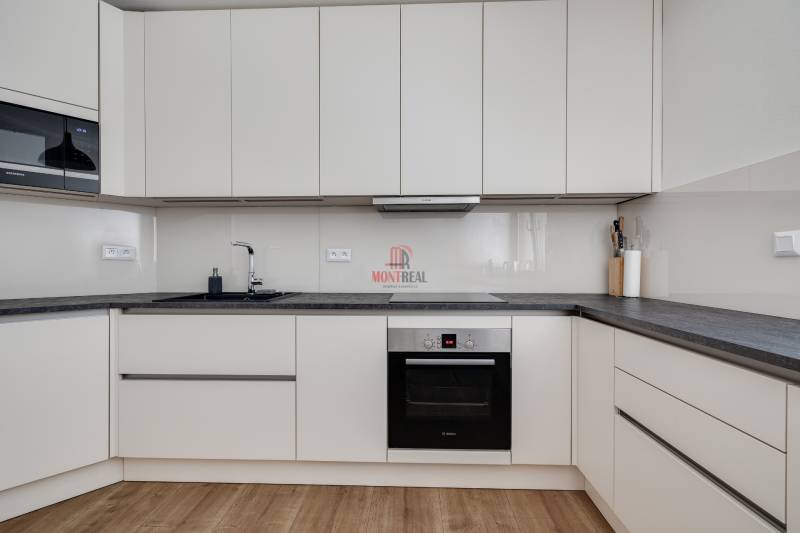 Küche in einer 3-Zimmer-Wohnung mit weißen Schränken und dunkler Arbeitsplatte.