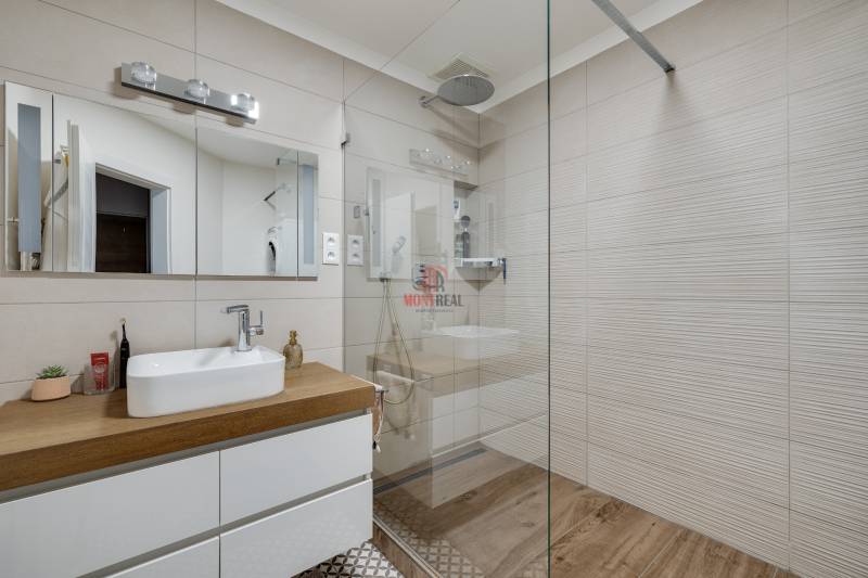Badezimmer mit weißem Waschbecken auf einer Holzplatte und großem Spiegel, 3-Zimmer-Wohnung.