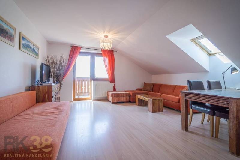 Ferienwohnung mit orangefarbenem Sofa und Esstisch unter dem Dachfenster.