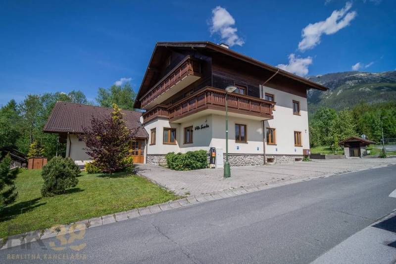 Ferienwohnung in der Hohen Tatra, umgeben von Grün, blauer Himmel, Berge im Hintergrund.