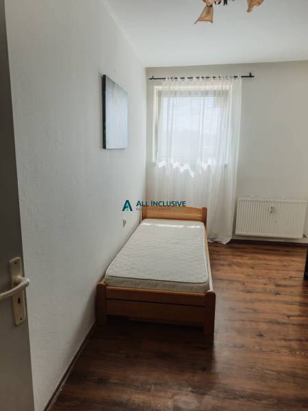 Einzelbett im Zimmer mit Fenster und Vorhang in einer Zweizimmerwohnung.