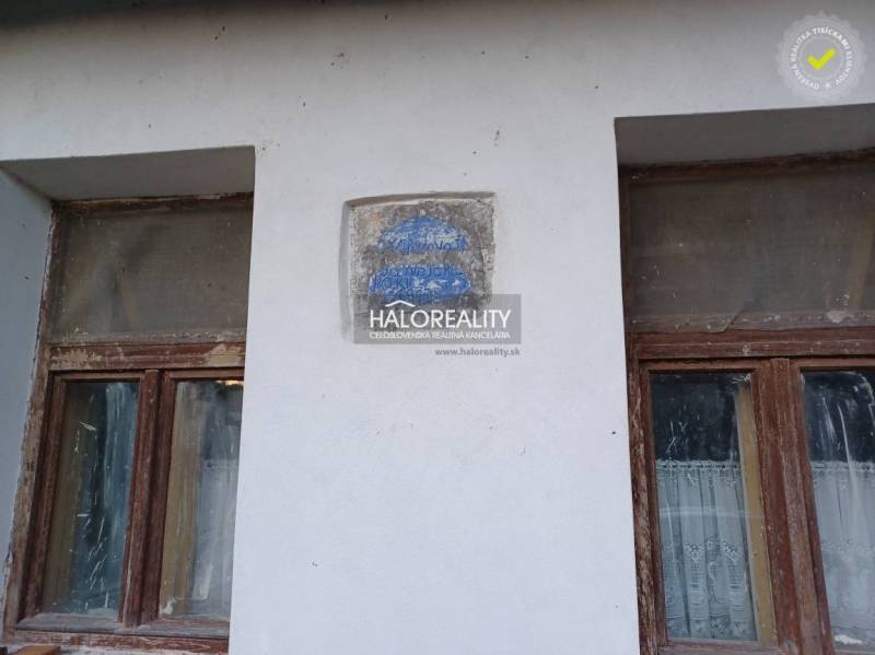 Zwei vernachlässigte Fenster eines Einfamilienhauses in Ladzany mit einem erodierten Schriftzug an der Wand.