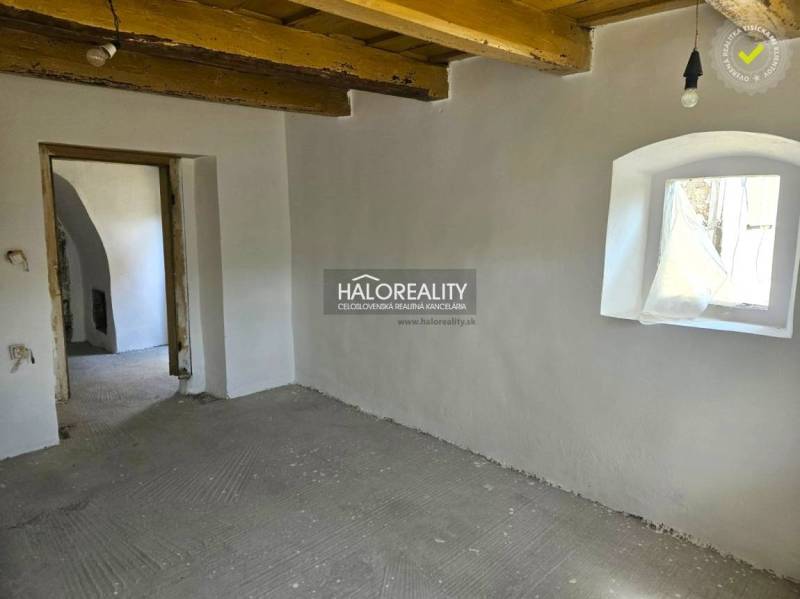 Innenraum eines Einfamilienhauses mit heller Wandfarbe, Holzbalkendecke und kleinem Fenster.