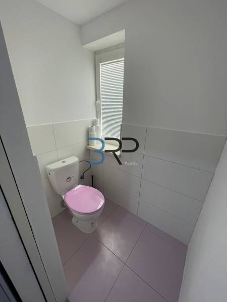 Badezimmer in einer 2-Zimmer-Wohnung mit einer rosa Toilette und weißen Fliesen.