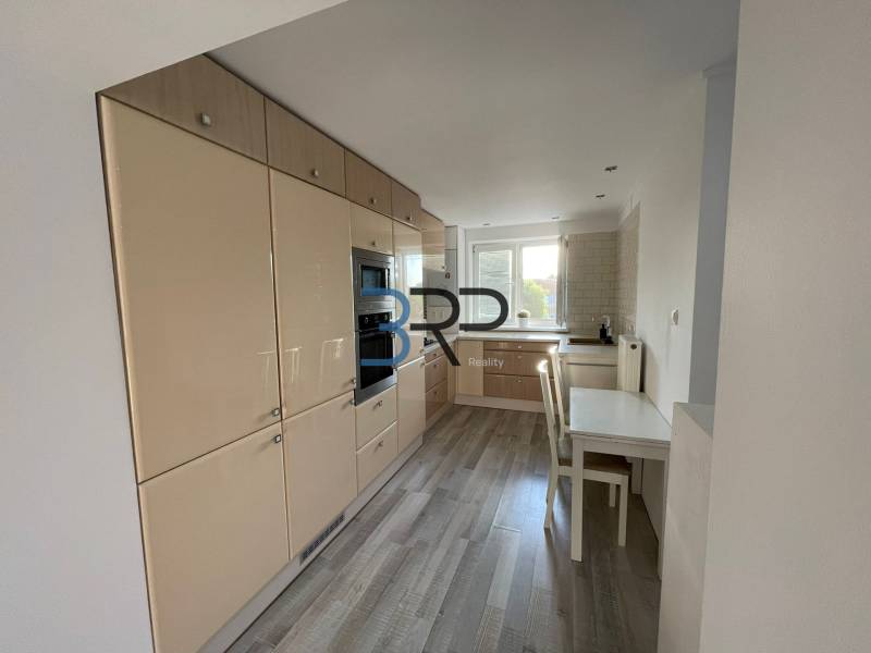 Küche in einer 2-Zimmer-Wohnung mit weißen Möbeln und Holzboden.
