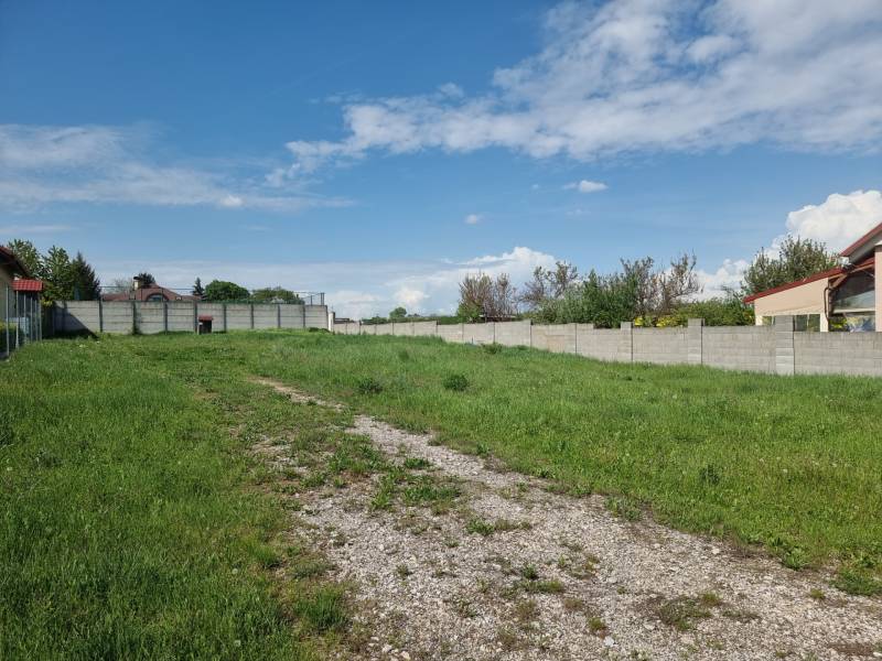Ein Baugrundstück in Cabaj-Čápor, umgeben von einer Graslandschaft und Zäunen unter blauem Himmel.