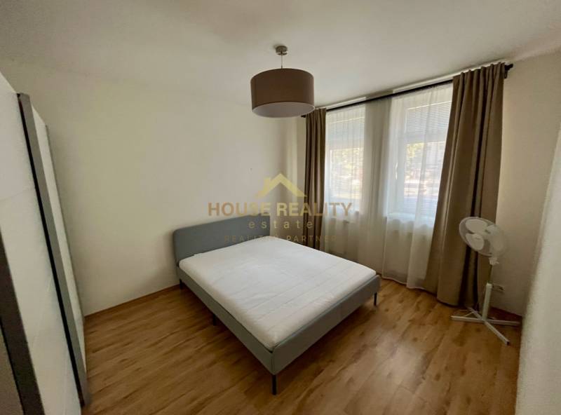 Helles Schlafzimmer mit Bett und Fenstern, 2-Zimmer-Wohnung mit Holzboden und Vorhängen.